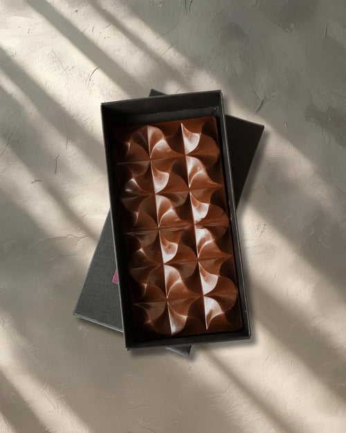 Chocolate bar with a geometric pattern in a black box on a textured surface