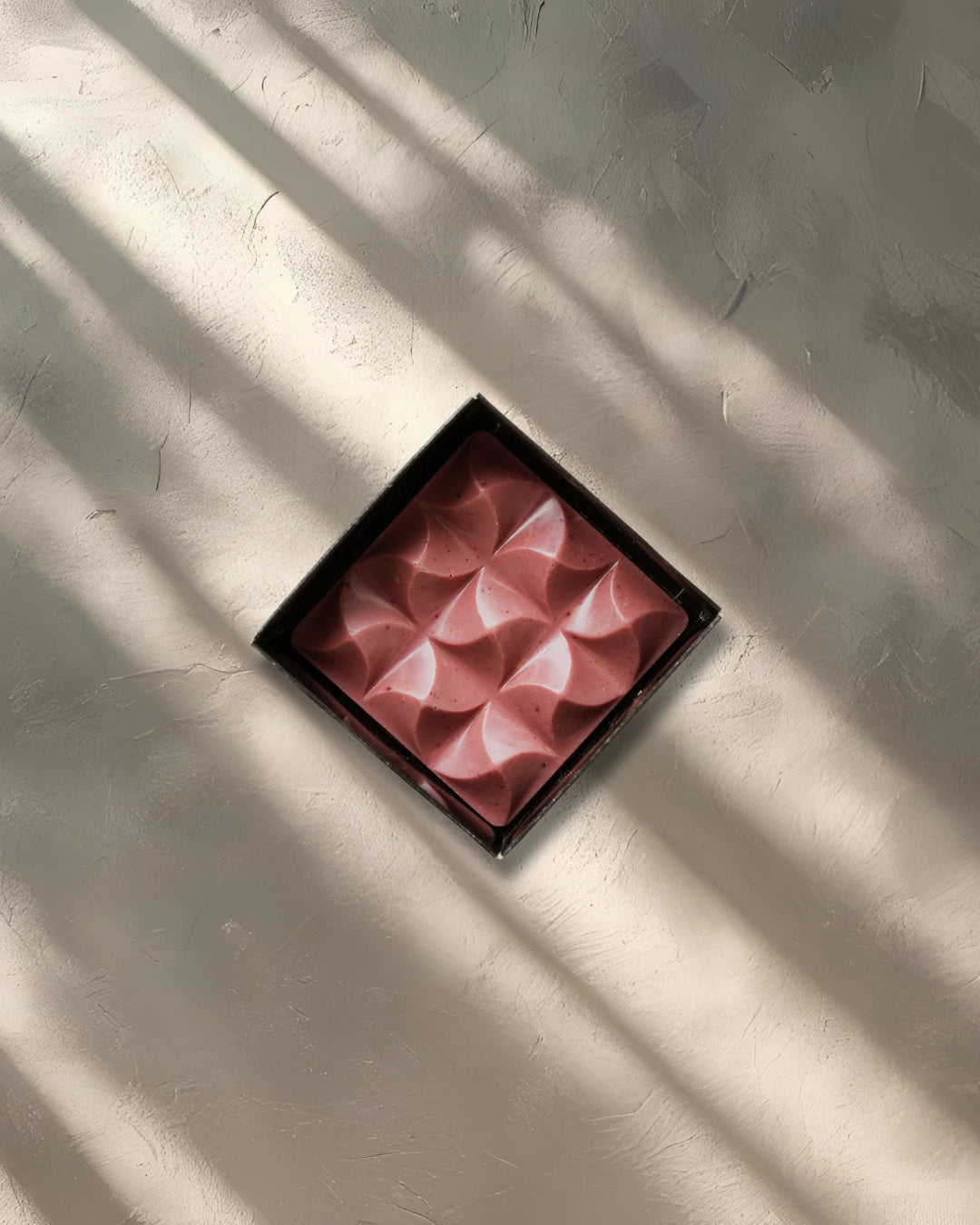Pink decorative item with a geometric pattern on a white wall with shadow patterns