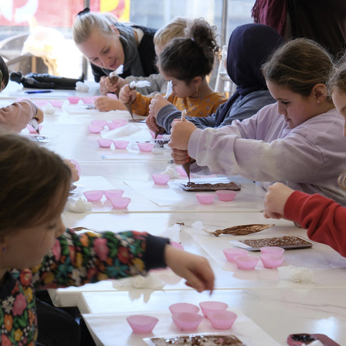 Children sitting at a long table making crafts in a classroom setting.